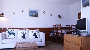 A cozy living room with a white sofa, wooden coffee table, and a dining area with chairs and a TV. - LARGE STUDIO 6 PEOPLE RESORT CENTER (LES ORRES 1650)