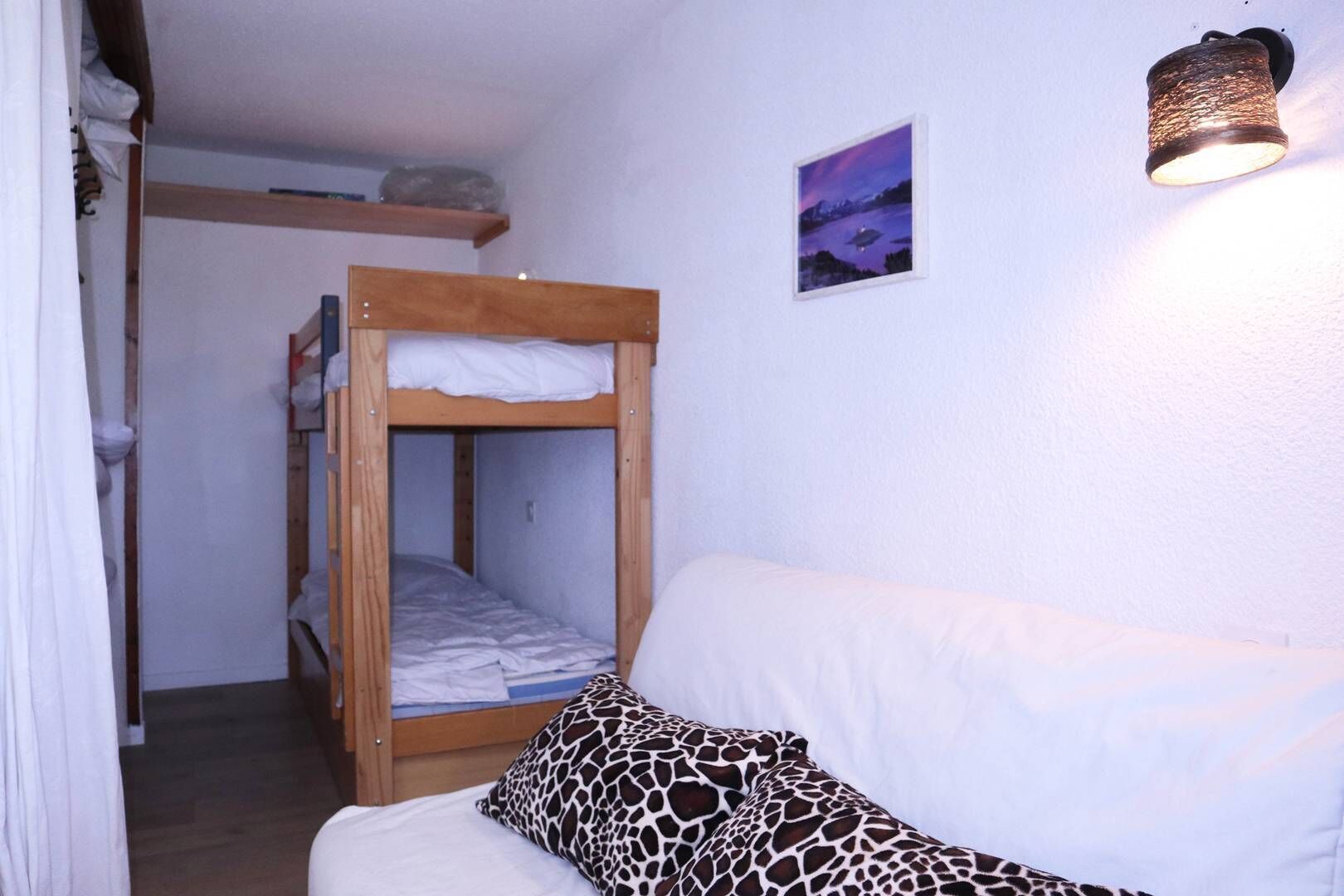 A small, cozy room with a bunk bed, a white sofa with a giraffe-patterned pillow, and a wall-mounted light fixture.