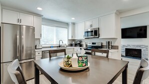 Una cocina moderna con electrodomésticos de acero inoxidable, armarios blancos y un comedor con una mesa dispuesta para dos personas.