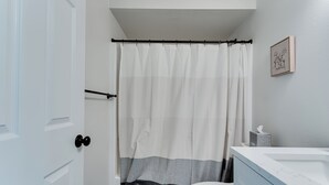 Un baño con inodoro blanco, tocador azul, cortina de ducha e imagen enmarcada en la pared.