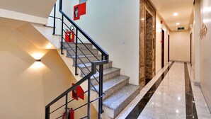A modern hotel interior with a marble staircase, black metal railings, and red fire safety signs.