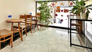 A hotel lobby with wooden chairs and tables, a potted plant, and a large window with floral decorations.
