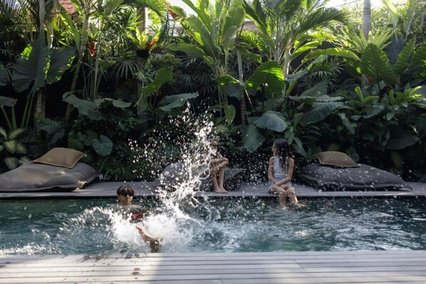 Uma área de piscina com um elemento aquático, cercada por vegetação exuberante e espreguiçadeiras.