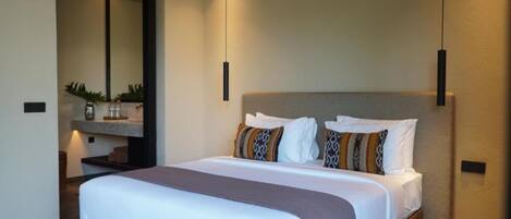 Habitación de hotel con una cama grande, cabecera, mesita de noche, espejo y lámpara fijada a la pared.