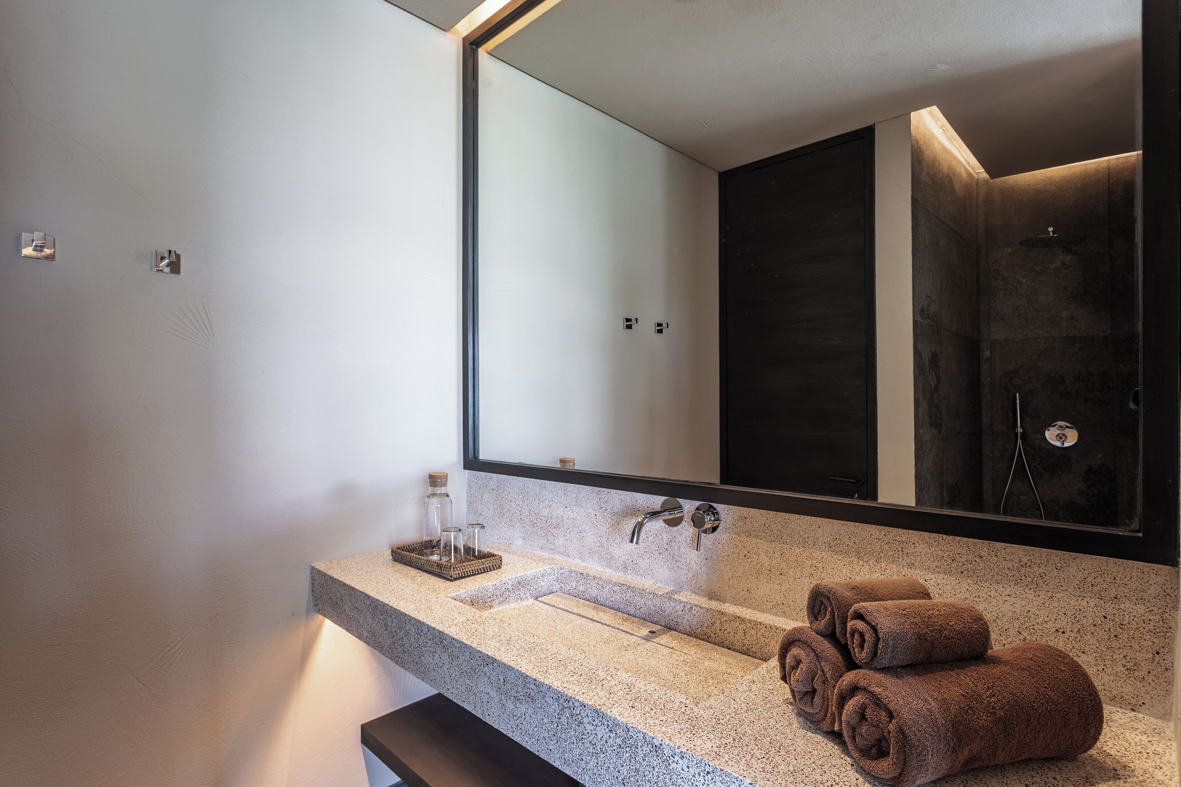 A modern bathroom with a large mirror, a granite countertop, and a dark shower area.