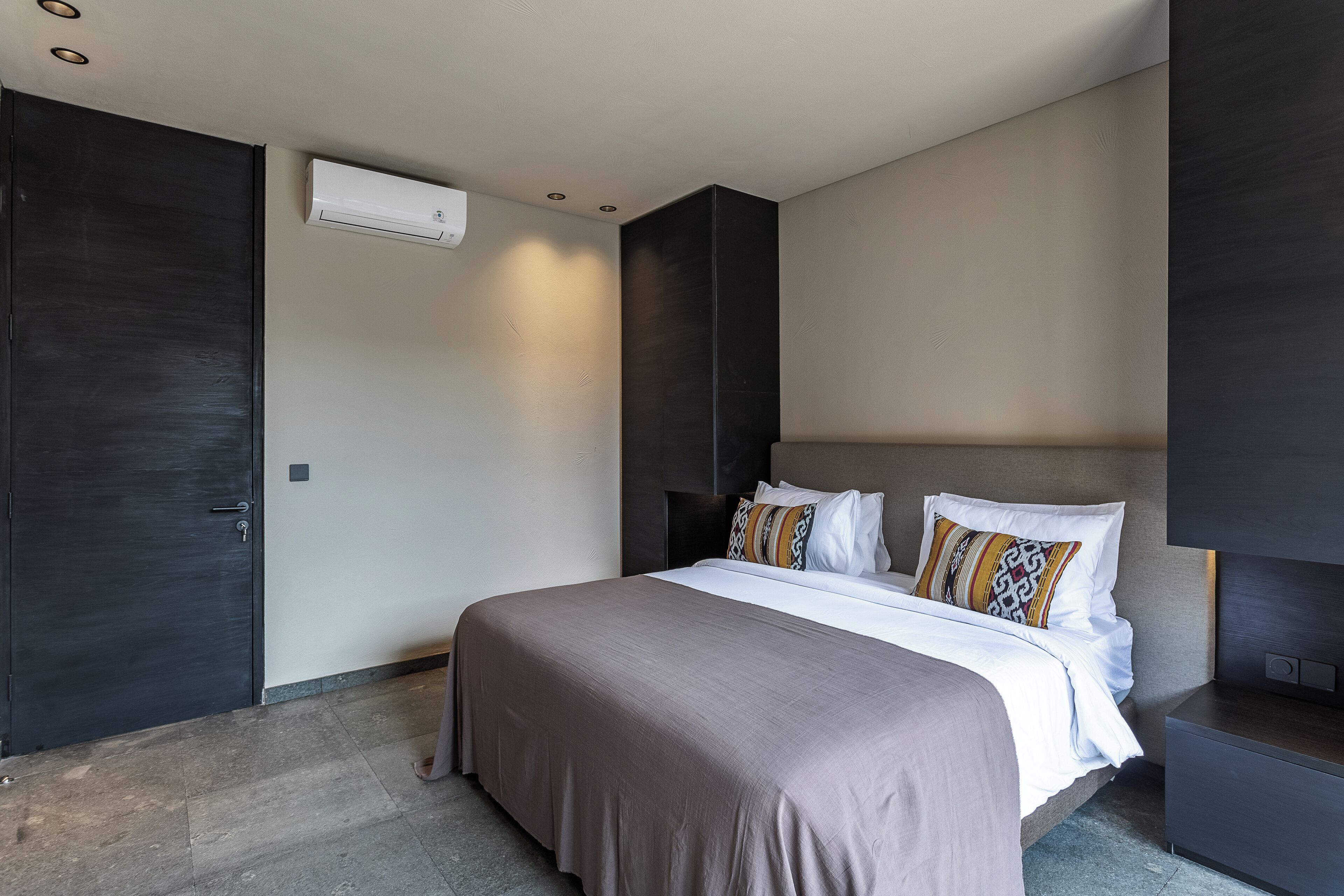 A modern bedroom with a large bed, dark walls, and a built-in TV.
