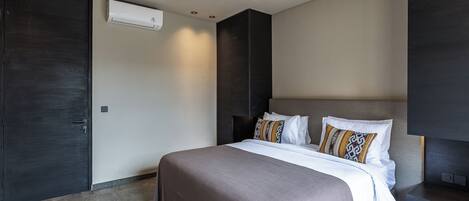 A modern bedroom with a large bed, dark walls, and a built-in TV.
