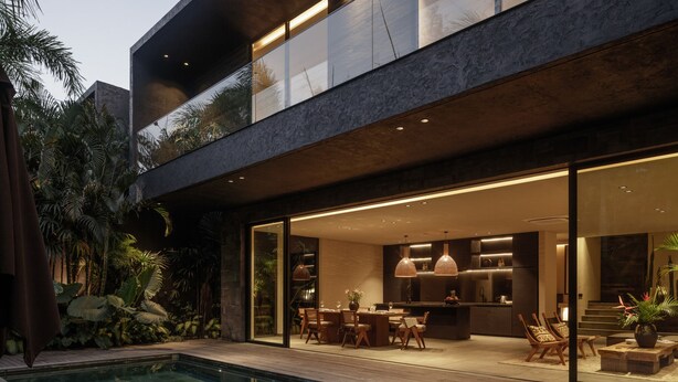 A modern house with a pool, outdoor dining area, and a kitchen visible through large glass doors.