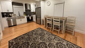 Una cucina moderna con mobili bianchi, elettrodomestici in acciaio inossidabile, un'area pranzo con tavolo e sedie in legno, e un tappeto decorato.