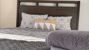 Un letto rifatto con cuscini decorati e una coperta patchwork, un quadro con una veduta urbana sulla parete e una coperta ripiegata sul letto.