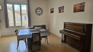 Ruokailuhuoneessa on puinen pöytä, tuoleja, piano ja seinäkello.