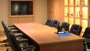 Un salón de conferencias con una larga mesa, varias sillas, una computadora portátil y un televisor en la pared.