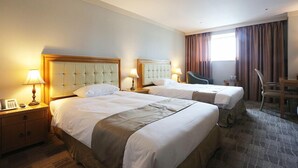 Una habitación de hotel con dos camas, un escritorio, una silla y un ventanal con cortinas.