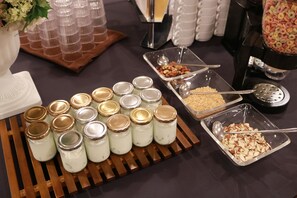 A buffet table with jars of food, a bowl of nuts, and a cereal dispenser.