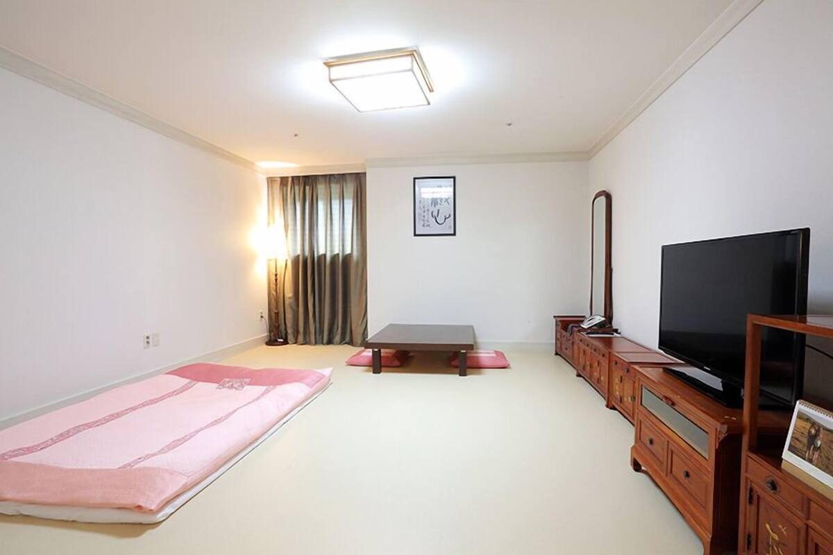 Um quarto com uma cama, uma televisão, um armário de madeira e um quadro na parede.