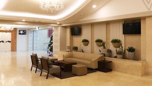 Un vestíbulo moderno con sofá, sillas, una mesa de centro, un candelabro y plantas en macetas.