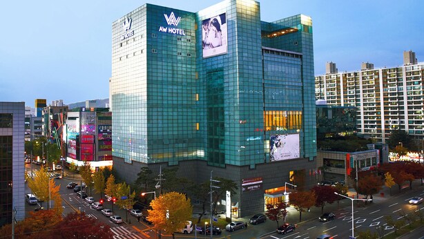 Un hotel moderno con fachada de vidrio, varios pisos y un llamativo letrero 'AW HOTEL'.