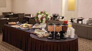 Montaje de bufé con diversos alimentos y bebidas, incluyendo un gran arreglo floral.