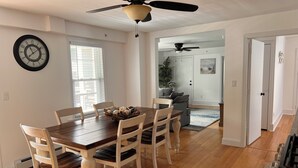 Un coin repas avec une table et des chaises en bois, un ventilateur de plafond et une horloge au mur.