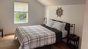 Une chambre à coucher comprenant un lit, un ventilateur de plafond, une fenêtre avec des stores, un gouvernail de bateau fixé au mur et une table de chevet avec une lampe.