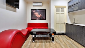 A compact living space with a red sofa, a small table, a mounted TV, and a kitchenette area. - HANZ Minh Thu Hotel Tan Binh (Ho Chi Minh City)