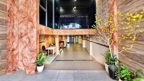 Un hall d’hôtel aux murs de marbre, avec un comptoir d’accueil, un espace salon et des plantes en pot.