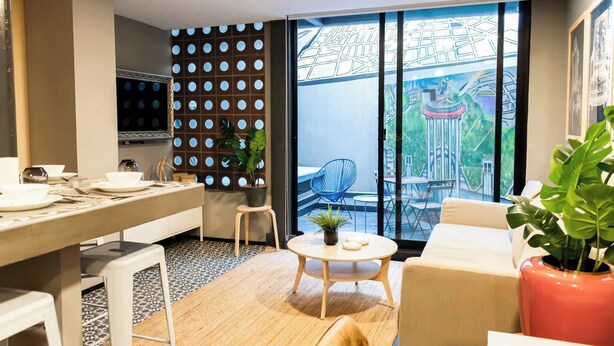 A modern living room with a dining area, a large window with a cityscape view, and a decorative wall with circular patterns. - Espectacular depto con terrazas en Condesa (Ciudad de México)