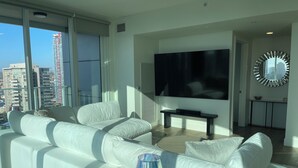 Una sala de estar moderna con un sofá blanco, un televisor de pantalla plana y un ventanal con vistas a la ciudad.