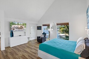 A bedroom with a bed, a white dresser, a chair, a window with a view of a body of water, and a door.