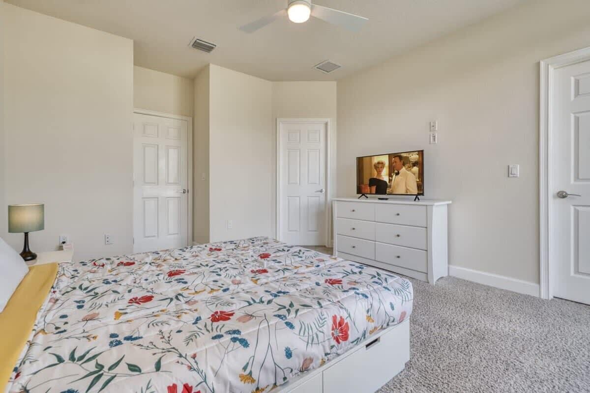 Een slaapkamer met een bed, een dressoir, een televisie en twee deuren.
