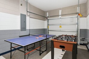 Ein Raum mit einem Tischtennisplatte, einem Kicker und einem Metallregal.