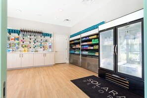 Un espace de vente moderne, avec des étagères remplies de divers produits, un présentoir réfrigéré et une porte donnant sur un autre espace.