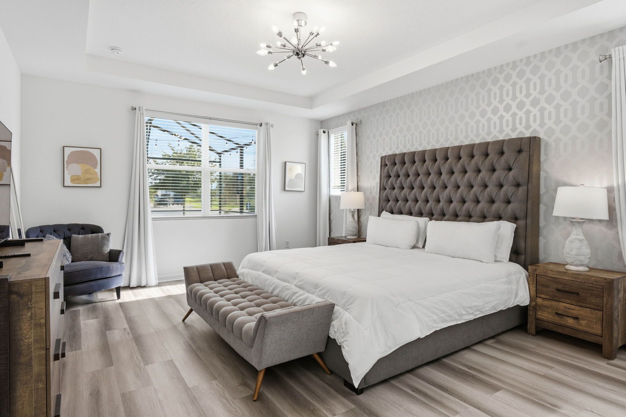 A modern bedroom with a large bed, a tufted headboard, a bedside table with a lamp, and a bench.