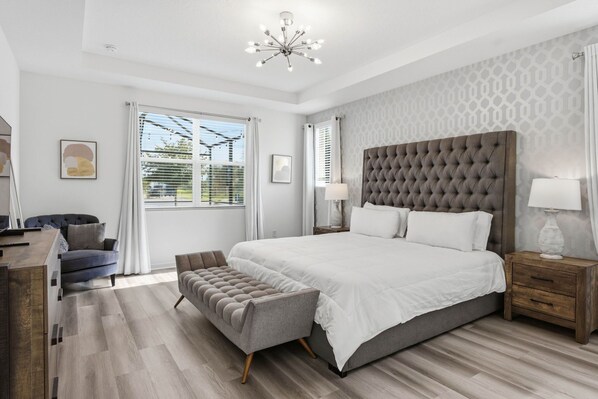 Une chambre à coucher moderne avec un grand lit, une tête de lit capitonnée, une table de chevet avec une lampe et un banc.