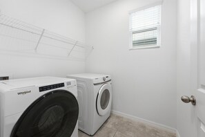 Une buanderie équipée d’un lave-linge Whirlpool et d’un sèche-linge Samsung, d’une fenêtre avec des stores et d’une porte dotée d’une poignée ronde.