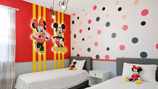 Un dormitorio con dos camas, una mesita de noche y un peluche de Mickey Mouse.