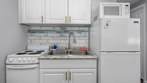 A kitchen with white cabinets, a stove, a sink, and a microwave. - Cozy Studio in the Heart of Downtown Kimmswick (Imperial)