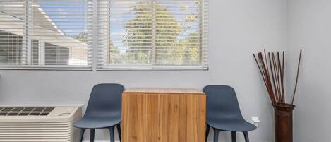 Een kamer met een houten tafel, twee stoelen, een radiator en een raam met jaloezieën.
