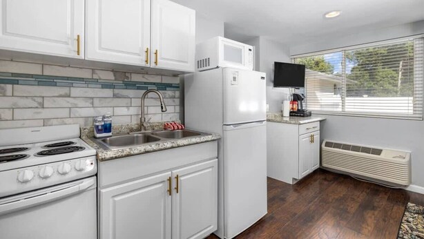 A modern kitchen with white cabinets, a built-in microwave, a stove, and a sink. - Cozy Studio in the Heart of Downtown Kimmswick (Imperial)