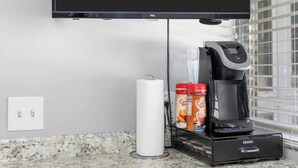 A kitchen with a flat-screen TV mounted above a countertop, a coffee maker, and a coffee machine. - Cozy Studio in the Heart of Downtown Kimmswick (Imperial)