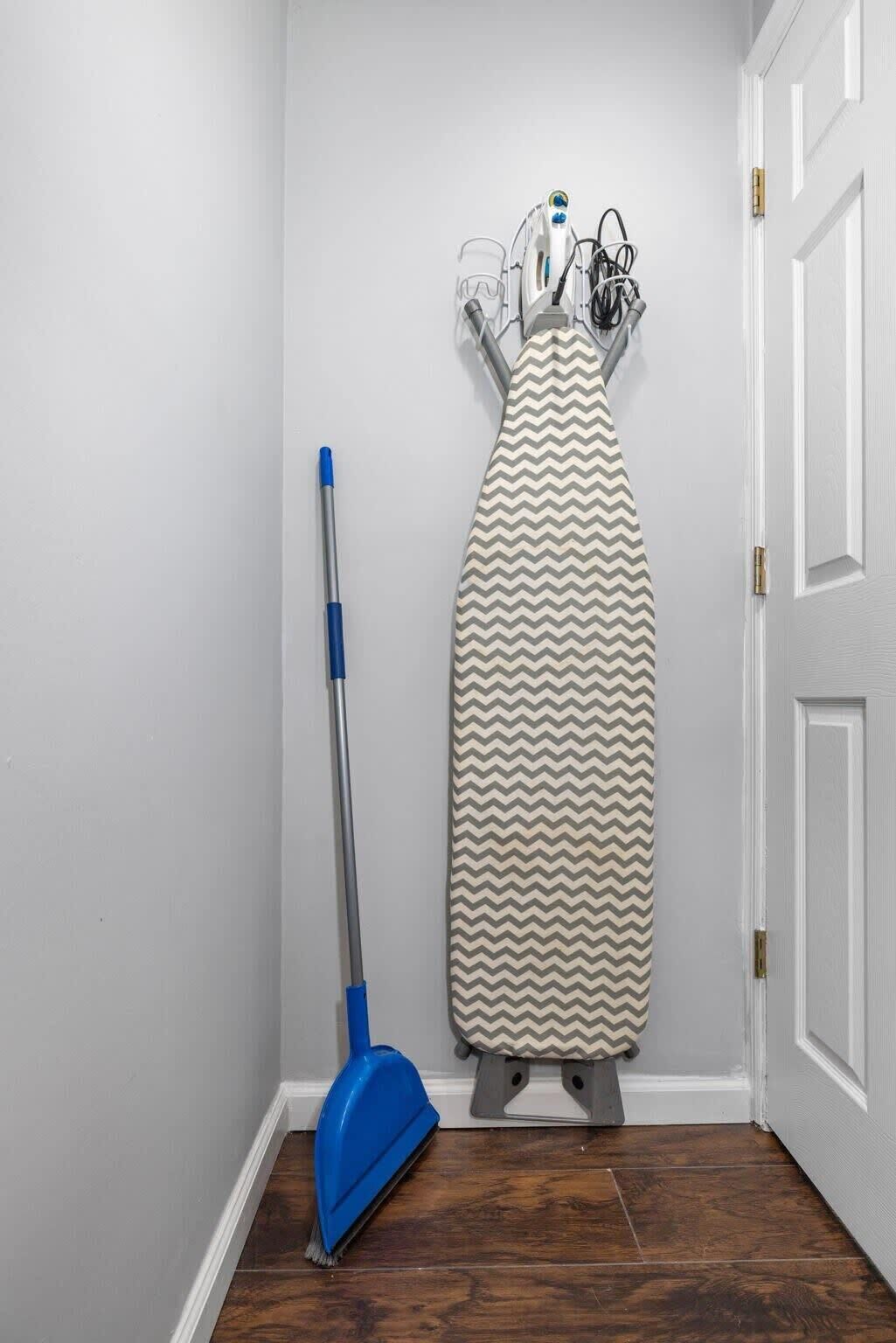 A room with a standing iron, a blue vacuum cleaner, and a white door.
