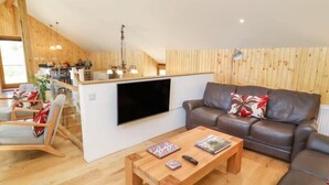 A cozy living room with a wooden floor, a brown leather sofa, a wooden coffee table, and a flat-screen TV mounted on a white wall.