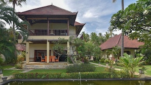 A two-story building with a tiled roof, surrounded by lush greenery and a small pond with a rock feature. - A quiet oasis in the traditional north of Bali right by the sea (Kubutambahan)