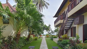 A pathway leading to a building with a balcony, surrounded by lush greenery and palm trees. - A quiet oasis in the traditional north of Bali right by the sea (Kubutambahan)