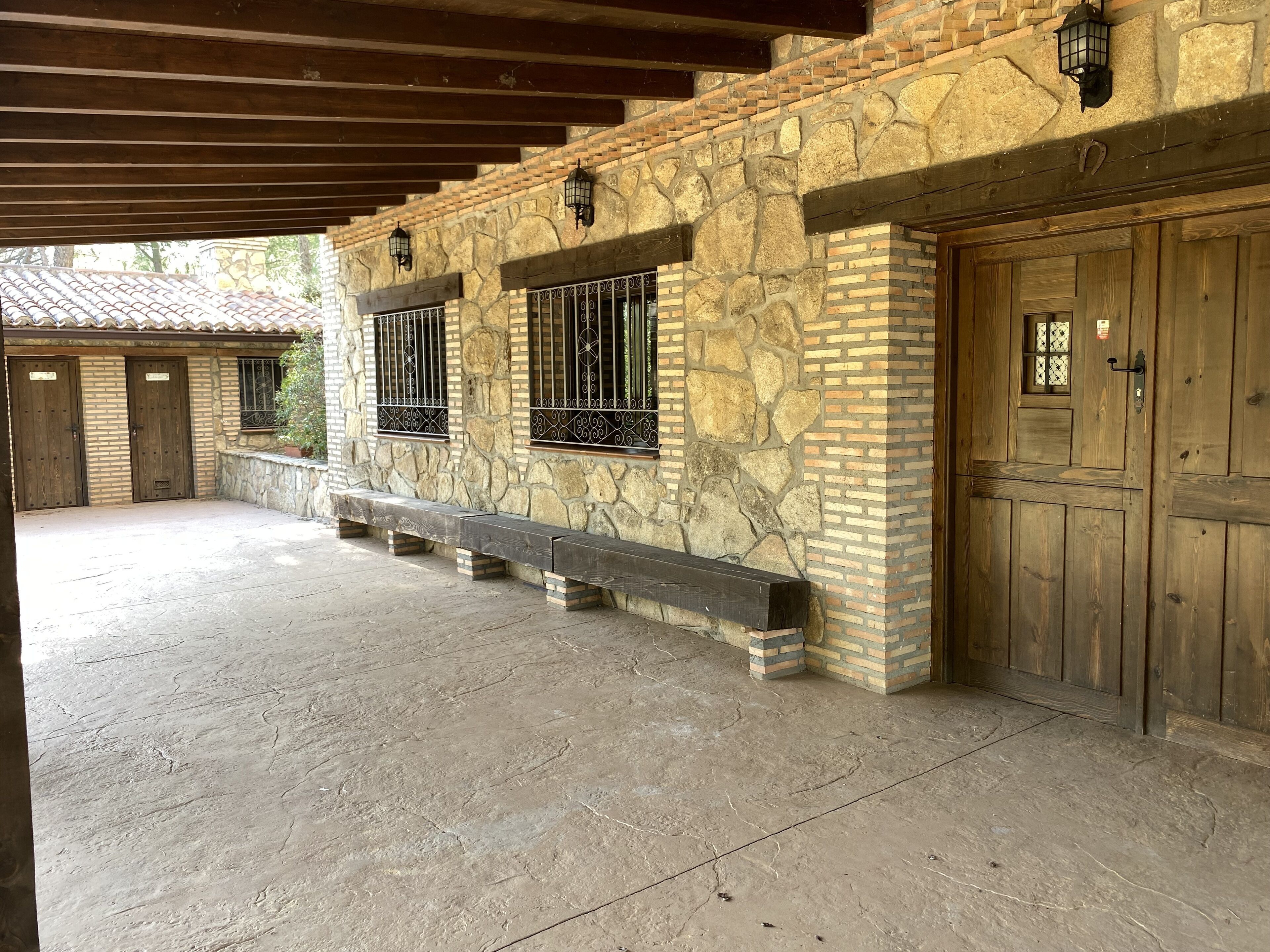 A stone building with wooden doors and windows, a bench, and a covered area.