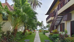 Un sentiero conduce a un edificio con un balcone, immerso nel verde e circondato da palme.