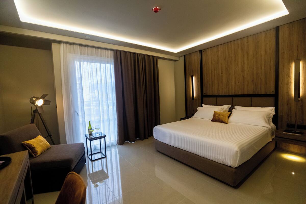 Une chambre d’hôtel moderne avec un grand lit, un bureau, une chaise et une petite table sur laquelle se trouvent une bouteille et des verres.