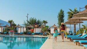 Zona junto a la piscina con sillas de descanso, sombrillas y cielo despejado.