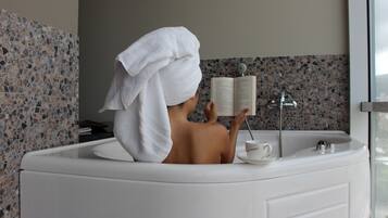 A person with a towel wrapped around their head sitting in a bathtub reading a book.