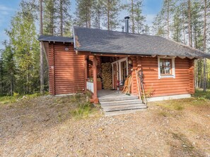 Een vakantiehuisje van hout met een houten veranda, een schoorsteen en een stapel hout voor de deur.